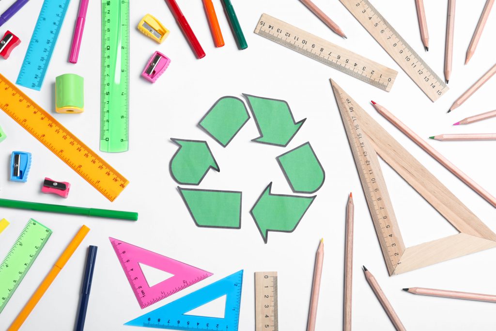 Plastikowe i drewniane przybory szkolne. Na środku symbol recyklingu.