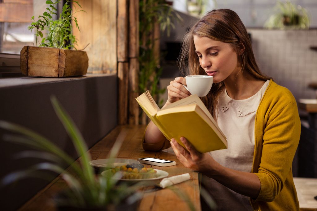 Kobieta pije kawę i czyta książkę w kawiarni
