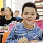 Uśmiechający się chłopiec, który siedzi w klasie. Wylosował on szczęśliwy numerek