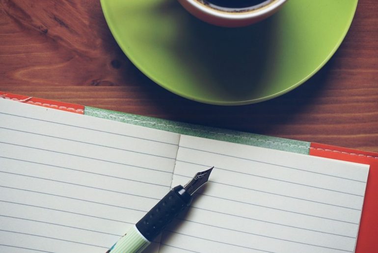 Zeszyt, pióro i kubek na blacie